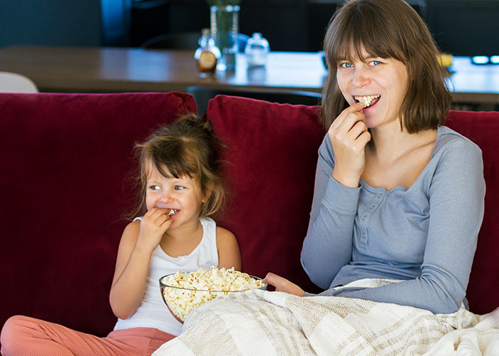 Mother and daughter enjoying popcorn on a red couch, illustrating unhinged mom hacks balancing genius and chaos.