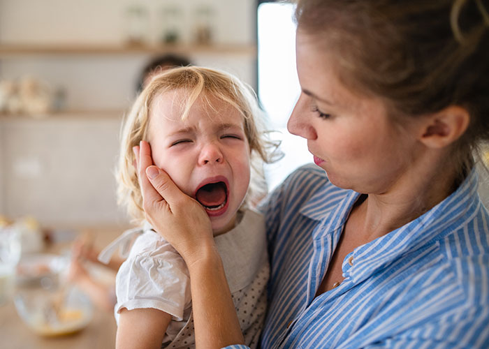 A mom calming her crying toddler in the kitchen, showcasing unhinged mom hacks that balance genius and chaos.