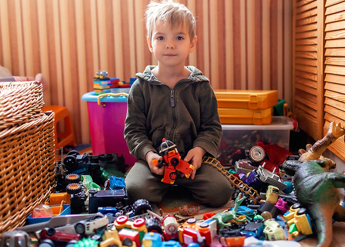 Young boy playing with toys in a cluttered room showcasing unhinged mom hacks that balance genius and chaos.
