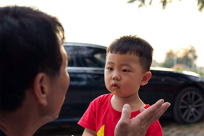 An older man giving street smart tips to a young boy outdoors near a parked black car at sunset.