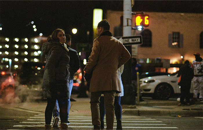 People walking and talking at a city crosswalk at night, illustrating street smart tips and tricks for urban safety.