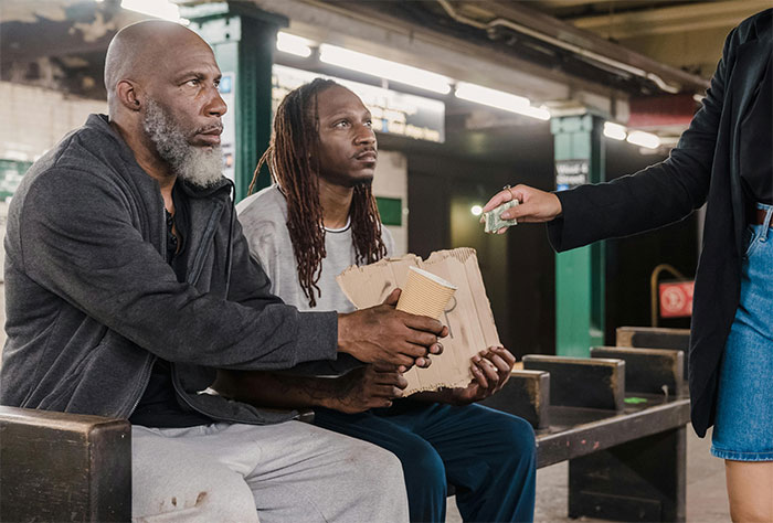 Two men sitting on a bench in a subway station receiving money and holding a cup and cardboard, representing street smart tips.