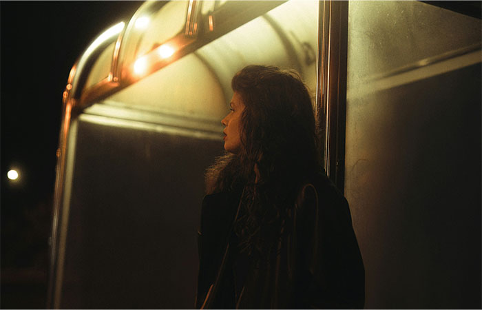 Woman standing alone at night under dim street lighting, reflecting a sense of street smart awareness and caution.