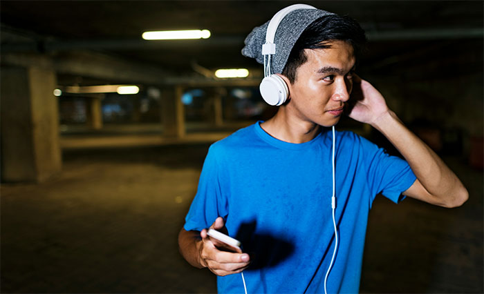Young man wearing headphones and holding smartphone in a dark urban setting representing street smart tips and tricks.