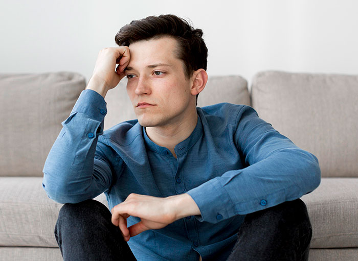 Young man in blue shirt sitting on floor, reflecting on reverse culture shocks after moving back home in America.