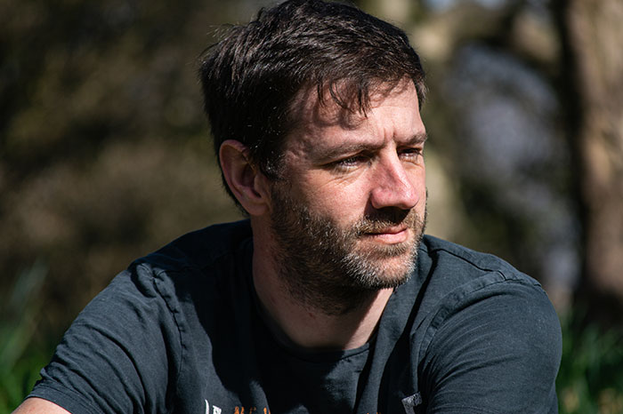 Man with beard and mustache outdoors, reflecting thoughtfully on reverse culture shocks experienced after moving back home.