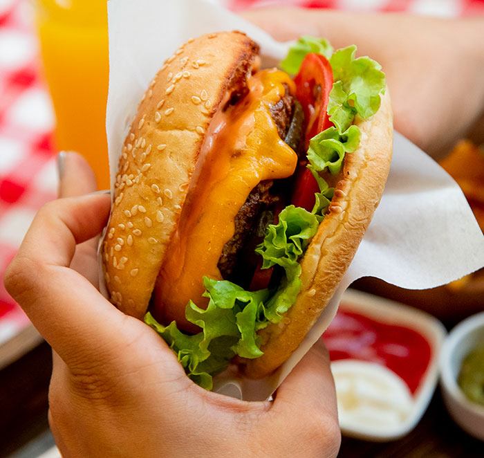 Close-up of a cheeseburger held in hand, illustrating American reverse culture shocks after moving back home.