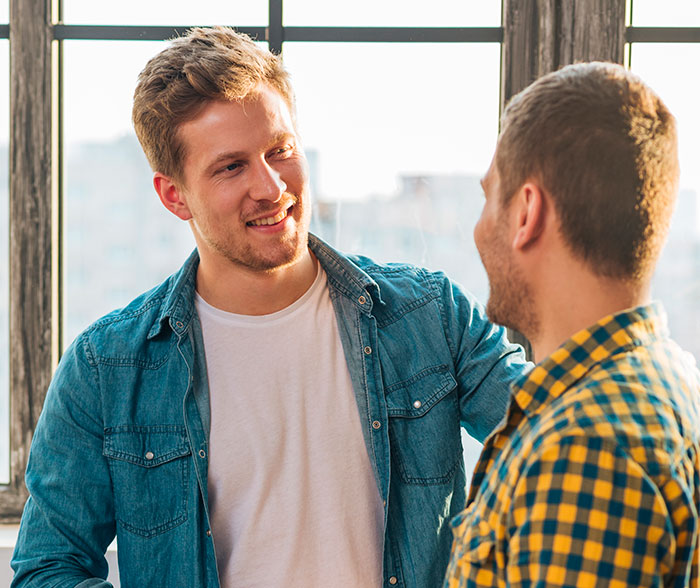 Two men having a friendly conversation by a window, illustrating Americans experiencing reverse culture shocks after moving back home.