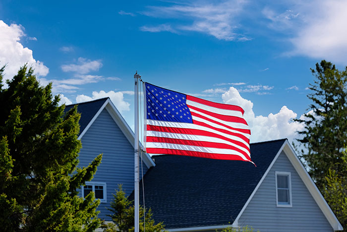 American flag waving in front of a house under a blue sky, reflecting reverse culture shocks experienced by Americans.