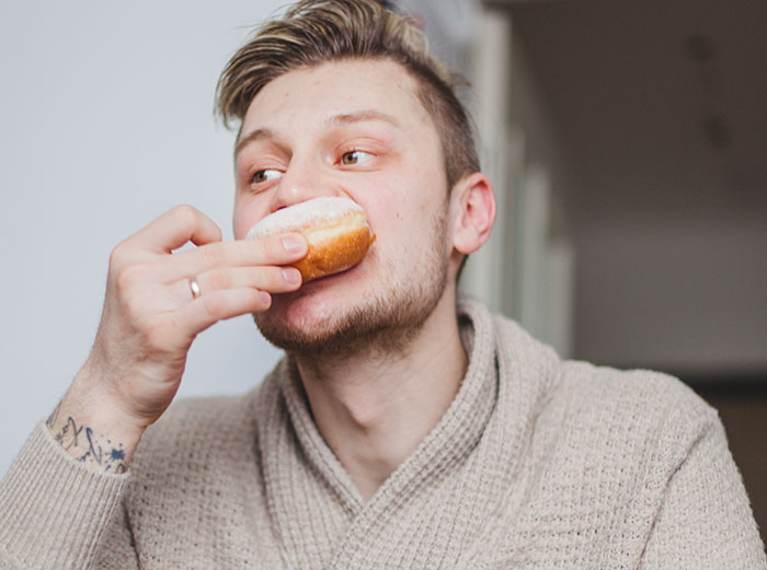 Young American man eating a doughnut indoors, illustrating a moment of reverse culture shock after moving back home.