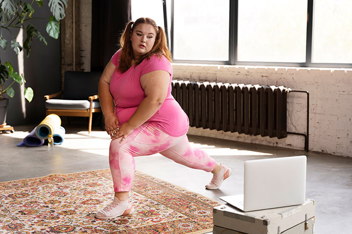 Plus-size woman exercising at home, stretching on a rug with laptop nearby, illustrating reverse culture shocks after moving back.