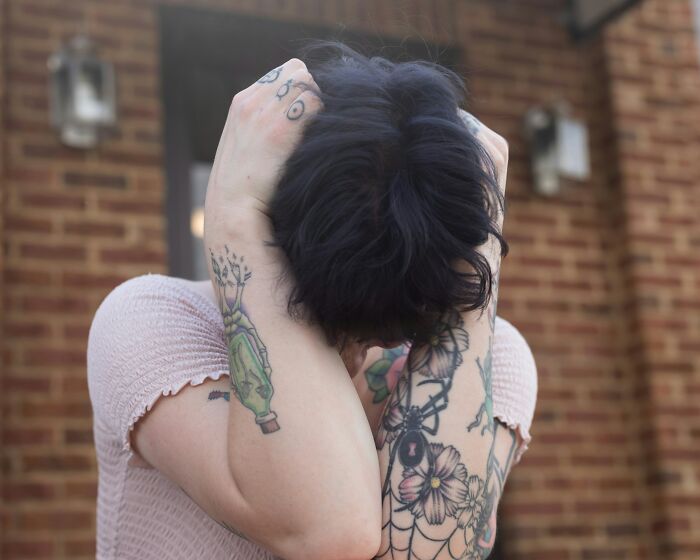 Person with tattooed arms covering their head, showing a moment of distress, reflecting Reddit not for the faint of heart.