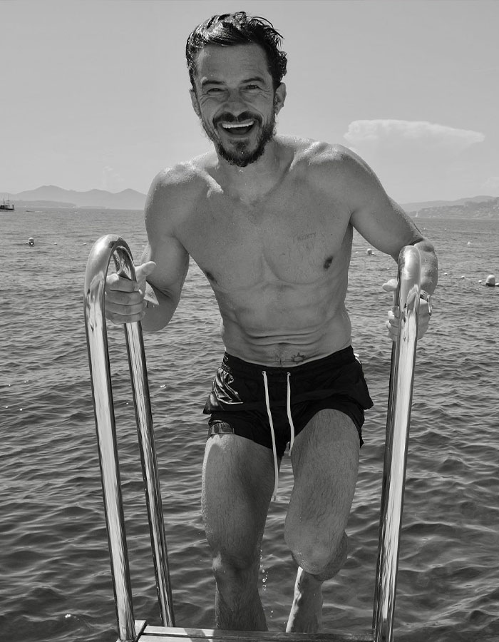 Orlando Bloom smiling and climbing pool ladder, trolling Katy Perry and Justin Trudeau dating rumors by the water.