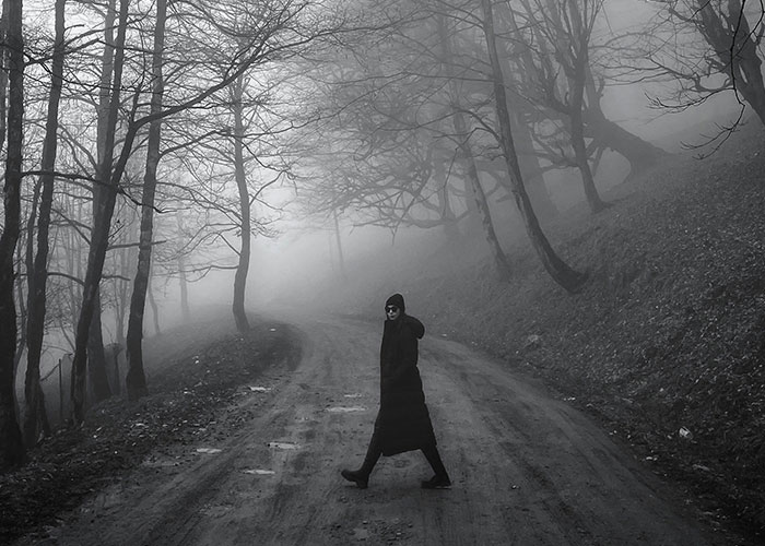 Person walking alone on a foggy dirt road surrounded by bare trees, evoking a tense and eerie job site atmosphere.