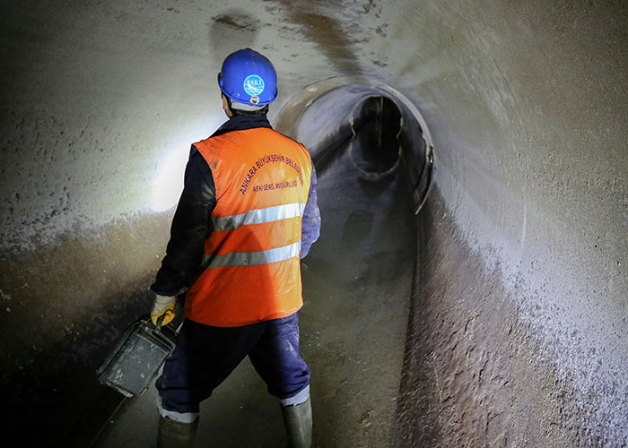 Worker in safety gear inspecting a dark, narrow tunnel at a job site, illustrating blue collar work hazards.