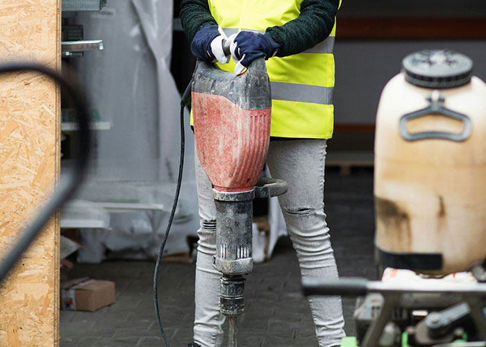 Construction worker in yellow vest operating heavy machinery at a job site, depicting blue collar workers' work hazards.