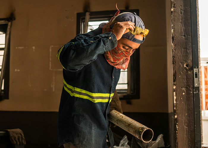 Blue collar worker wearing protective gear and holding a pipe at a job site, showing workplace safety awareness.