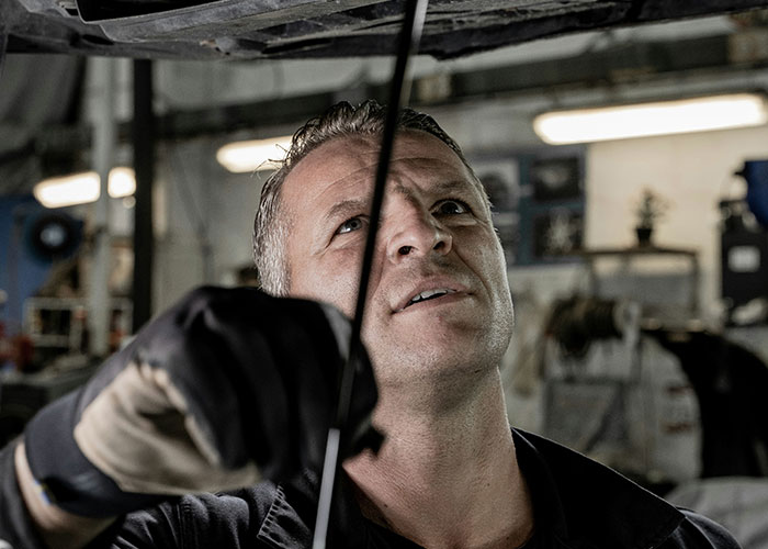 Blue collar worker wearing gloves inspecting machinery in a dimly lit industrial job site environment.