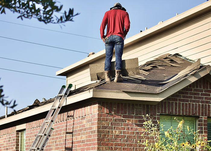Blue collar worker standing on a damaged roof near a ladder, illustrating a scary job site moment.
