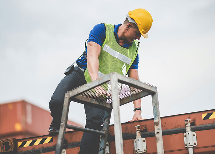 Construction worker wearing safety gear climbing a ladder at a job site, highlighting blue collar worker safety risks.