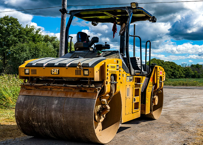 Yellow Caterpillar road roller parked on a job site under a partly cloudy sky, illustrating blue collar workers' risky experiences.