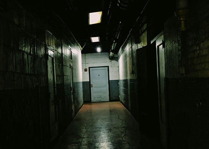 Dimly lit industrial corridor with concrete floors and walls, evoking a tense atmosphere on a blue collar job site.