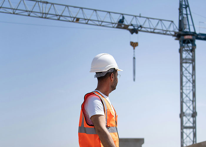 Construction worker in a hard hat and safety vest looking at a crane at a job site, highlighting blue collar worker safety.