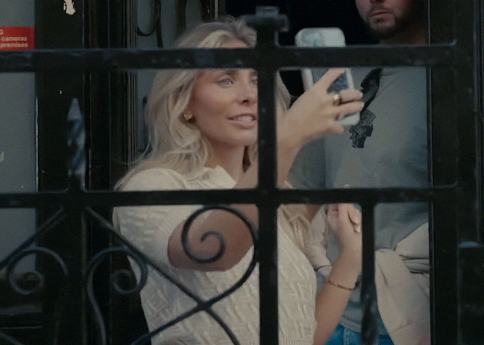 Woman changes expression while taking a selfie behind a window, body language expert analyzes the moment in a scandalous doc. - 3