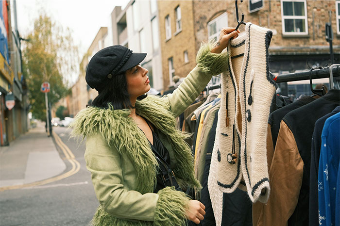 Woman in green fur coat examines trendy clothing at outdoor market, highlighting profitable industries in fashion retail.