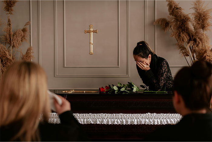 Mourning woman at a funeral home placing roses on a casket, illustrating profitable funeral industry trends today.