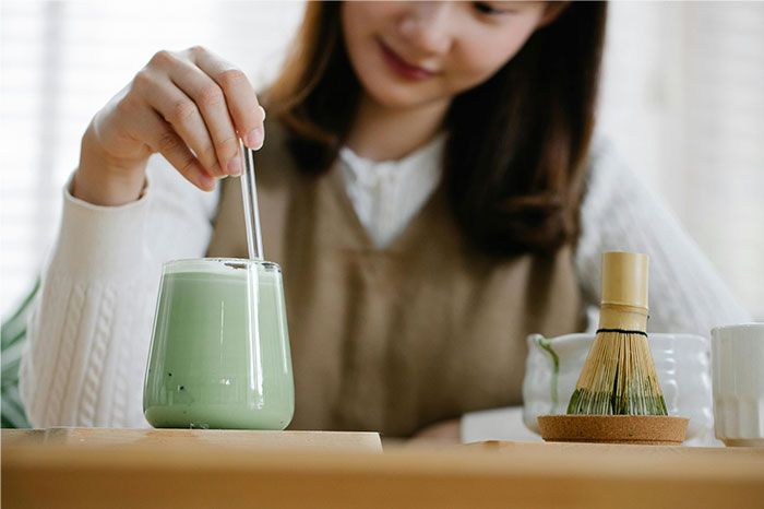 Woman preparing a green tea drink with traditional tools, illustrating profitable industries in food and beverage sectors.