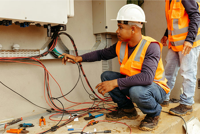 Electrician in safety gear working on wiring inside a control panel, highlighting profitable industries these days.