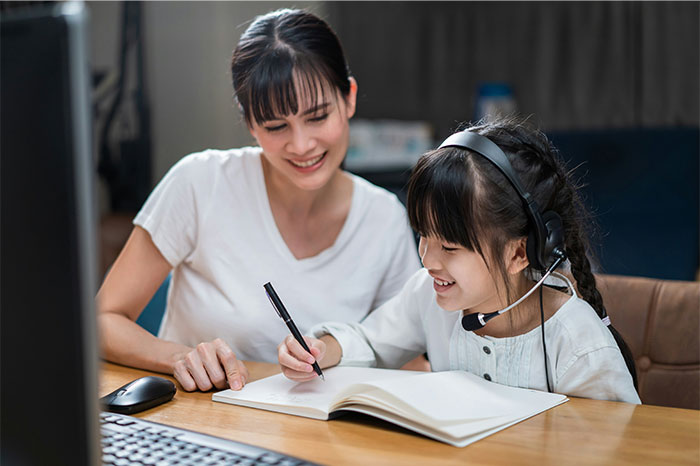 Woman helping child with homework wearing headset, illustrating profitable industries in education and online learning.