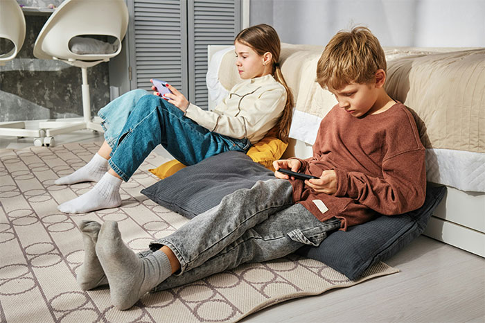 Two children sitting on cushions playing mobile games, illustrating profitable industries in entertainment and technology.