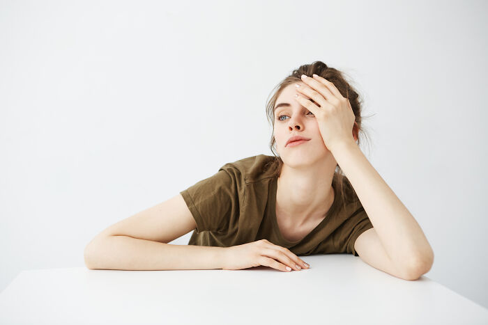 Young woman in a green shirt looking tired and frustrated while resting her head on her hand, representing words not in English.
