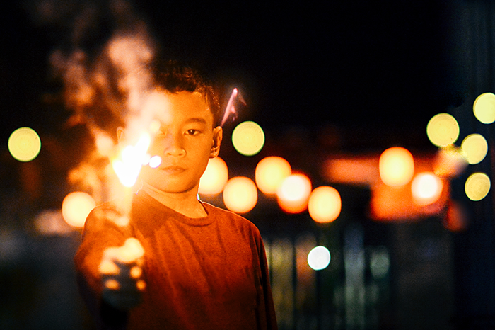 Boy holding a sparkler at night with glowing lights in the background, illustrating grieving son and family conflict.