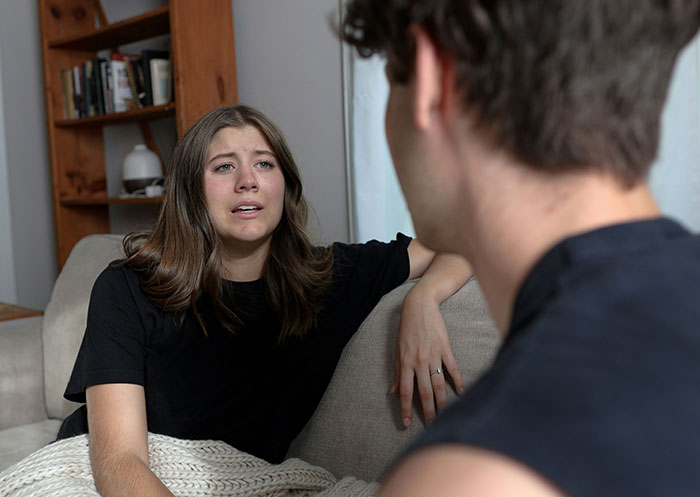 Woman faces double heartbreak, emotional while revealing boyfriend&rsquo;s true character after mother&rsquo;s death in a living room setting.