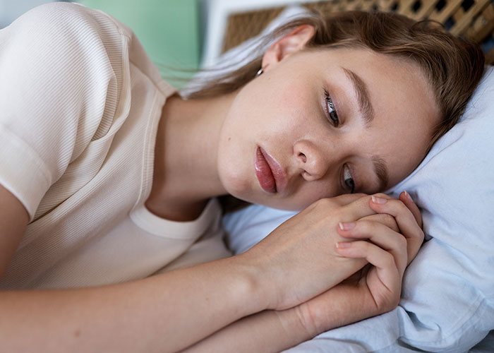 Young woman lying on bed, appearing thoughtful and distressed, reflecting on cancer related to HPV and relationship challenges.