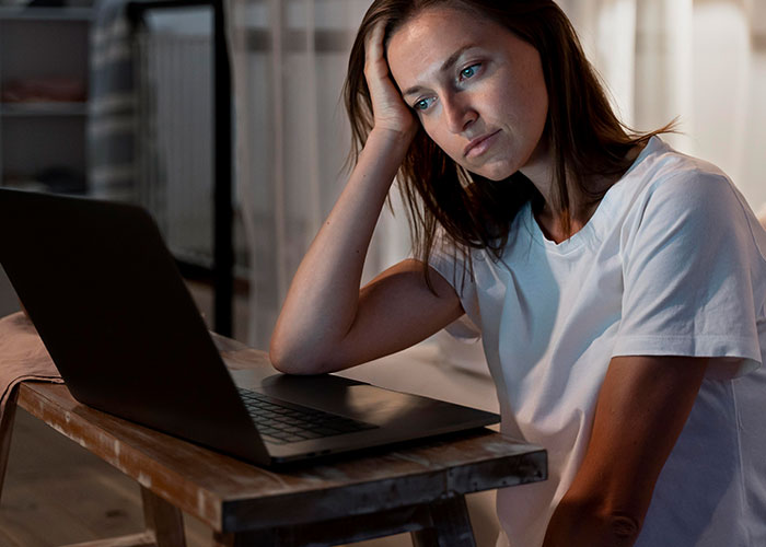 Woman with cancer feeling resentful while using laptop, reflecting on healthy boyfriend and past HPV diagnosis.