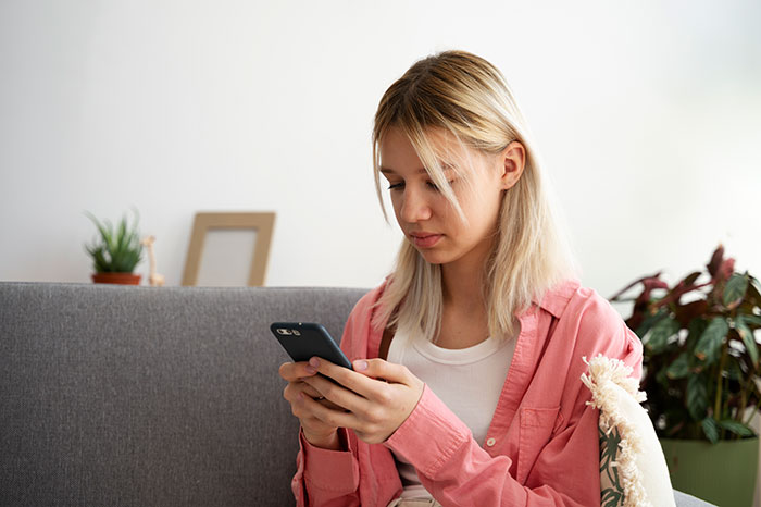 Young woman looking upset while holding a phone, suggesting confrontation after guy pretends to be single at party.