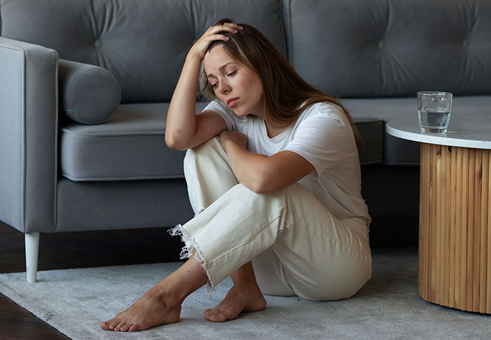 Young woman sitting on floor looking upset and stressed after boyfriend pretends to be single at party
