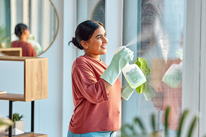Woman cleaning window with gloves and spray, illustrating challenges of keeping a clean toddler in family relationships.