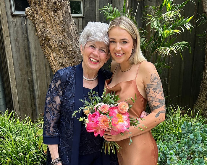 Two women smiling outdoors, one holding a bouquet of flowers, representing Brad Pitt's final public message to his mom. Two women smiling outdoors, one holding a bouquet of flowers, representing Brad Pitt's final public message to his mom.