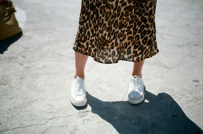 Person wearing leopard print skirt and white sneakers standing outdoors, highlighting gender-based double standards in fashion.