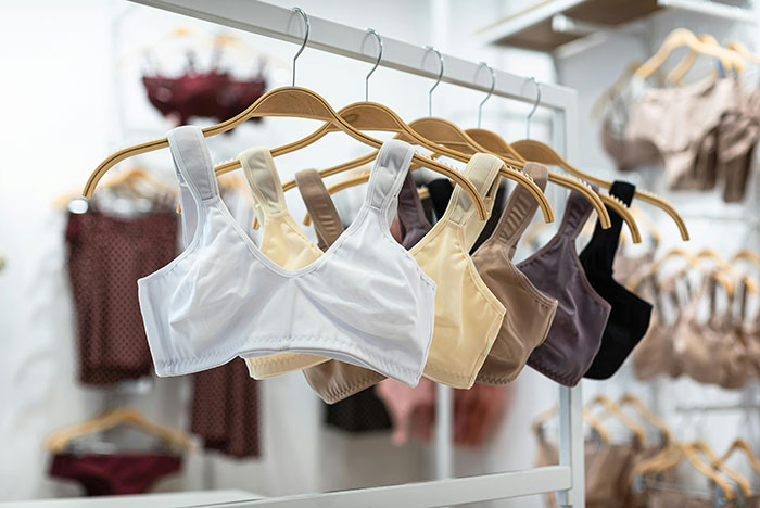 Bras in various neutral colors hanging on wooden hangers in a retail store, highlighting diverse styles and comfort.