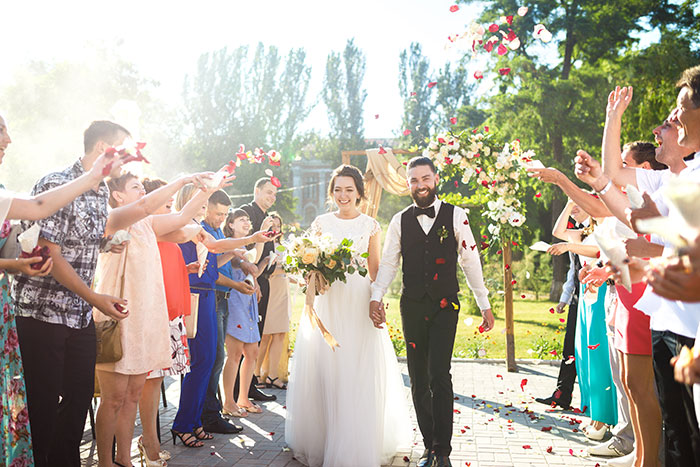 Bride and groom walking through guests throwing petals at an outdoor wedding with chaos and crime scene implications.