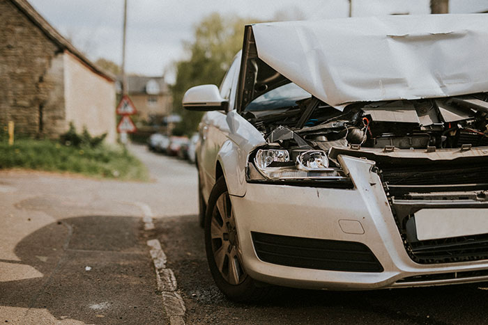 Damaged white car with crumpled hood parked on a street, hinting at chaos and a crime scene after a wedding incident.