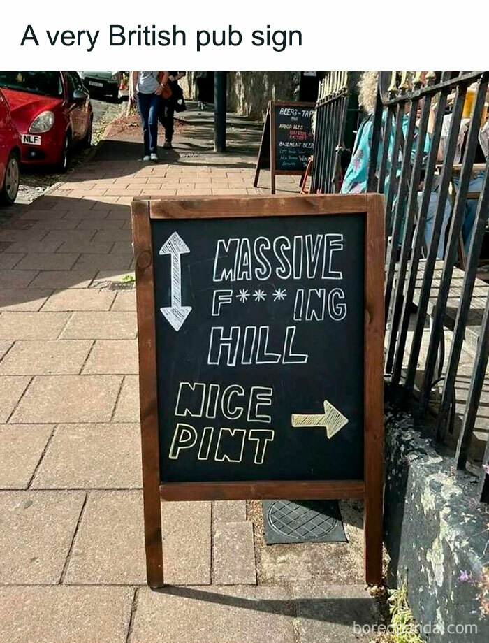 Chalkboard sign outside a British pub humorously warning of a massive steep hill and pointing to a nice pint.