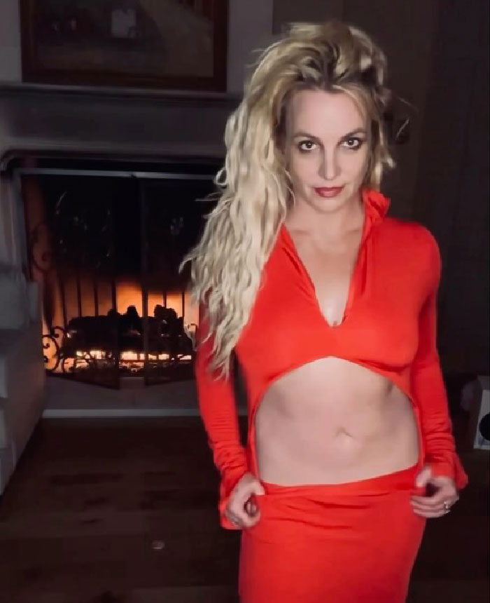 Britney Spears posing indoors in a red outfit with a fireplace in the background, fans reacting to Kevin Federline memoir news. Britney Spears posing indoors in a red outfit with a fireplace in the background, fans reacting to Kevin Federline memoir news.