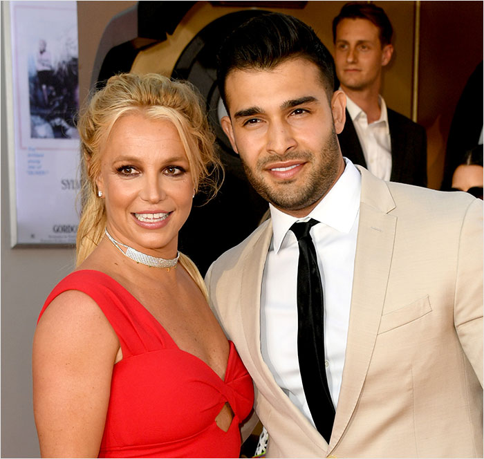 Britney Spears wearing a red dress posing with a man in a beige suit and black tie at a formal event.